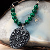 Pendant from a fashion statement necklace made of black clay with a flower imprint.